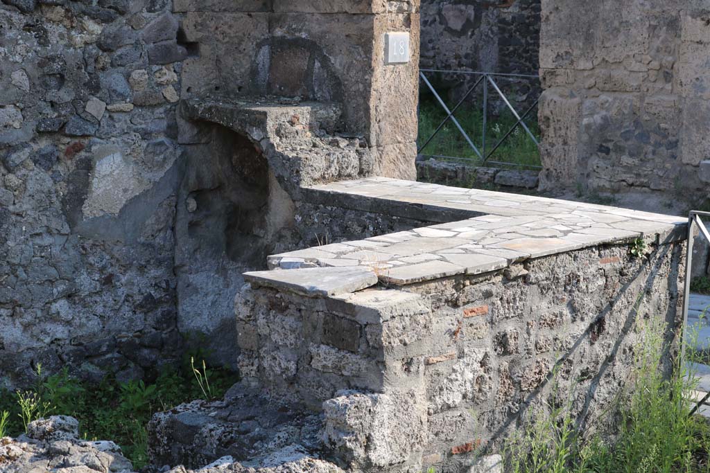 VI.1.18, Pompeii. December 2018.
Looking south-west across hearth at east end of two-sided marble counter and two-tier shelving. Photo courtesy of Aude Durand.