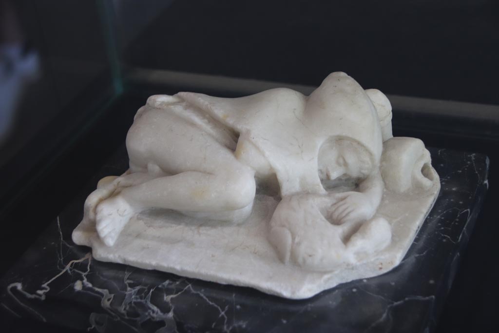 VI.2.22 Pompeii. October 2022. Marble statue described as “Young fisherman asleep”, found in the house but location unknown.
On display in the Palaestra. PAP Inventory number 21628. Photo courtesy of Klaus Heese.
According to Jashemski –
“The two marble statuettes found in the house would probably have been garden decorations: a deer suckling her young (0.21m long) and a sleeping child whose left hand holds the handle of a basket which a mouse tries to enter. Behind the boy’s head an overturned vase (0.19m long) poured water. The mask found in the house may also have decorated the garden.”
See Jashemski, W. F., 1993. The Gardens of Pompeii, Volume II: Appendices. New York: Caratzas. (p.122-3)