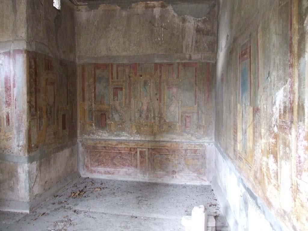 VI.7.23 Pompeii. December 2006. Cubiculum decorated with mythology of Apollo. West alcove, looking to west wall.
According to E. Winsor Leach, the scene in the rear alcove has long posed a challenge to identification.
Set in a gabled aedicula intricately patterned with shining gold fretwork, the figure of Apollo enthroned beneath the canopy identifies this setting as the palace of the sun.
Less certain are the identity of 2 figures, one male and one female, positioned at either side of the god.
The most commonly accepted proposal has been a contest between the Morning and Evening Stars.
Although nothing is wrong with this idea, Moorman has proposed a plausible and more interesting identification as representing Euripides’ tragedy Phaeton, which takes place in Apollo’s palace.
Several fragments survive from this lost drama, which Wilamovitz reconstructed as centring about a projected marriage between Phaeton and Aphrodite, which Phaeton’s earthly parents, Merops and Clymene, had contrived in exploitation of his semi divine status as Apollo’s son.
Kenneth Reckford has recently given a new interpretation of the story line in which one of the daughters of Helios will have been substituted for Aphrodite as a bride.
The reconstructed plot has Phaeton sent to Apollo’s palace to claim his bride whom nonetheless he rejects, asking instead to drive Apollo’s chariot for his proof of paternity.
The scene on our scaenae frons shows Phaeton confronting his designated bride in Apollo’s throne room.
See Leach, E. Winsor, 2004. The Social Life of Painting in Ancient Rome and on the Bay of Naples. Cambridge UK: Cambridge UP, Fig 80, page 121.