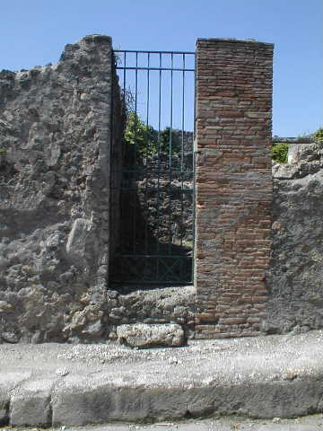Lead pipe in pavement between VI.15.3 and VI.15.4 on Vicolo dei Vettii.
The pipe goes through the wall of VI.15.4. December 2007.