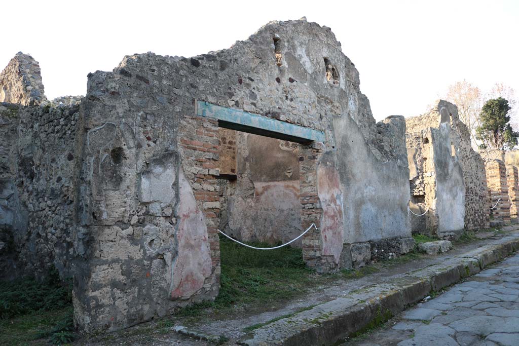 VI.15.11 Pompeii. May 2005. West wall of shop, with doorway into rear room. The rear room was linked to the atrium of VI.15.12. According to Boyce, on the east wall in the room behind the shop, was a very crude lararium painting. In the upper zone stood the Lares in the usual attire and position, between them was the Genius. In the lower zone were two serpents confronted at an altar furnished with two eggs. In the background were plants. Below the serpents, there were roughly sketched drawings of a ham, a hog’s head, sausages, and other foods.
Above the panel and hanging down on each side, were painted garlands. Not. Scavi, 1897, 199.  See Boyce G. K., 1937. Corpus of the Lararia of Pompeii. Rome: MAAR 14. (p.55, no.217, and Pl.22, 2)
See Fröhlich, T., 1991. Lararien und Fassadenbilder in den Vesuvstädten. Mainz: von Zabern. (L72, he said it was destroyed and no longer visible)




