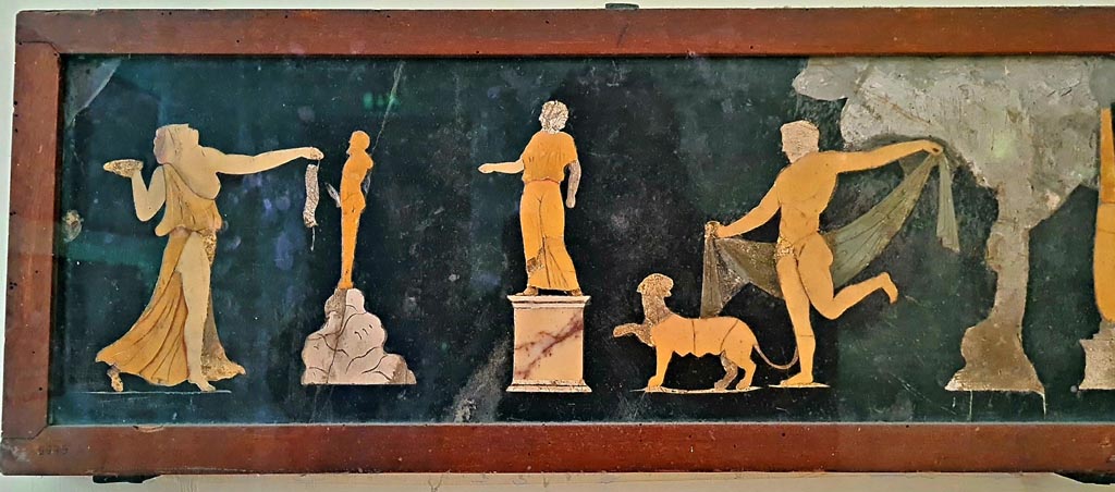 VII.4.31/51 Pompeii.
Found in tablinum on 22nd May 1845. Dionysian scene in coloured marble. Photo courtesy of Giuseppe Ciaramella. September 2024.
Now in Naples Archaeological Museum. Inventory number 9979.
According to information card –
Dionysian scene. Slate wall panel with polychrome marble inlay work.
A statue on a pedestal is depicted in the centre of the scene; Dionysus, dressed in a cloak, is dancing on the right, preceded by a panther; on the left, a Maenad, who is also dancing, brings offerings to a statue of Priapus, placed on a rock. (Third quarter of the Ist century AD).
(Scena dionisiaci. Panello parietale di ardesia con intarsia marmorei policromi.
La scena raffigura, al centro, una statua su piedistallo; Dioniso con mantello danza, da destra, preceduto da una pantera; mentre da sinistra, una Menade pure danzante reca offerte alla statua di Priapo, posto su una roccia. Terzo quarto del I secolo d.C.)
