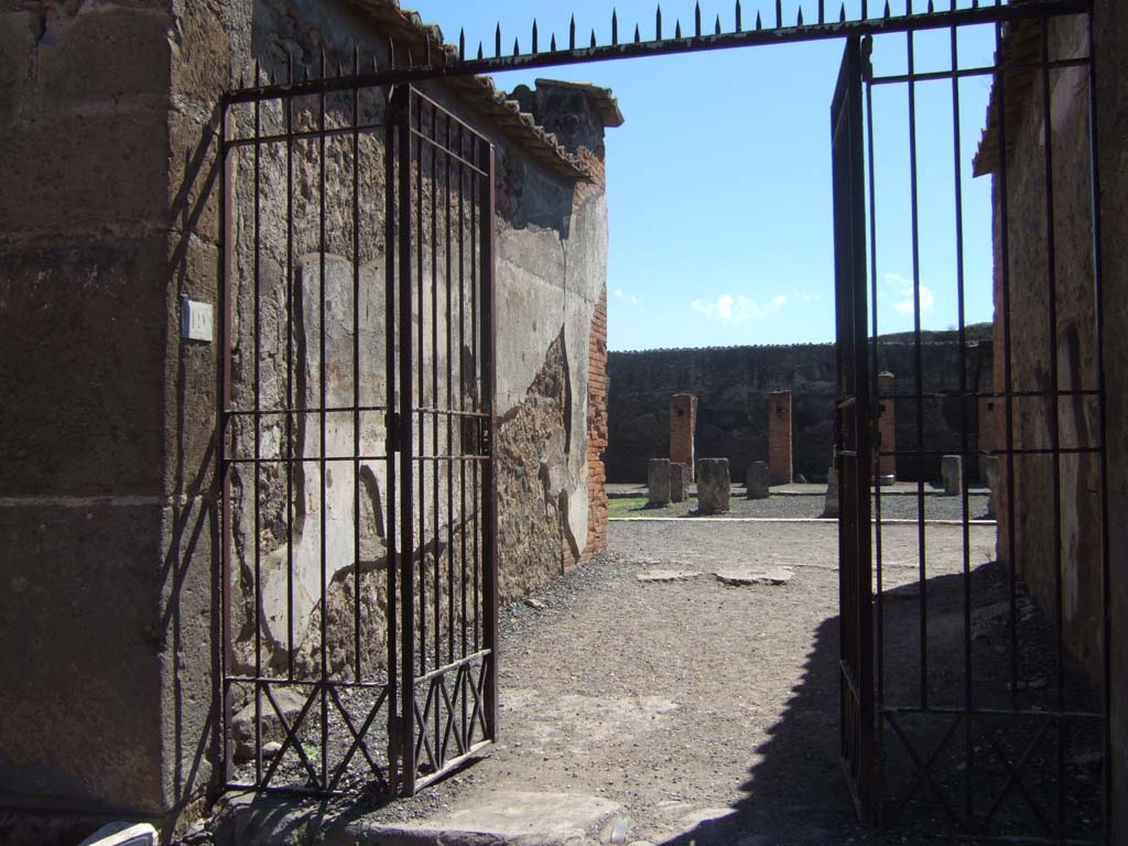 VII.9.19 Pompeii. September 2005. North entrance to Macellum on Via degli Augustali, looking south.
According to Mau, somewhere amongst these shops and stalls to the north of the macellum, various charred foodstuffs were found.
Charred figs, chestnuts, fruits in glass vessels, plums, grapes, lentils, grain, loaves of bread and cakes were excavated.
See Mau, A., 1907, translated by Kelsey, F. W., Pompeii: Its Life and Art. New York: Macmillan.