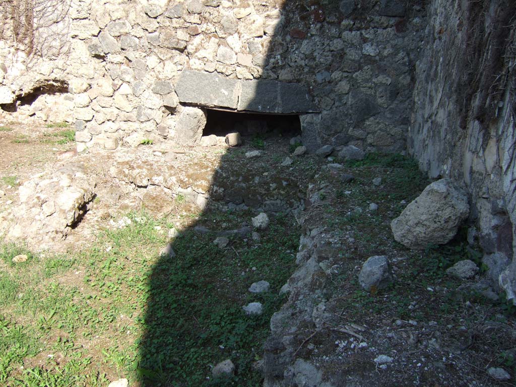 VII.12.7 Pompeii. September 2005. Looking east to remains of oven and work-bench near south wall. According to Boyce, on the south wall of the room with the oven was a large lararium painting. In the centre was a blazing tripod, with the Genius to the right of it. On each side was a wreathed Lar. To the left of this group stood Vesta, at her side was an ass with a bell around its neck. On the right of the group stood Mercury.
In the lower zone, marked off from the upper by a brownish stripe, were the two serpents. They were approaching a gold-coloured altar, on top of which was a white shallow dish containing a blazing fire. In the fire was an egg and several fruits – a date, a pomegranate and a medlar.
See Boyce G. K., 1937. Corpus of the Lararia of Pompeii. Rome: MAAR 14. (p.70, no.313)
See Helbig, W., 1868. Wandgemälde der vom Vesuv verschütteten Städte Campaniens. Leipzig: Breitkopf und Härtel. (68)