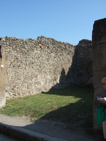 VII.12.10 Pompeii. September 2005. South wall with rear room of shop.
On the right, were the stairs to upper floor and corridor to rear yard.
According to Boyce, in the south-west corner of the rear area was a lararium. In the west wall of the kitchen above the hearth was the lararium painting. It depicted the usual sacrificial scene of the Genius assisted by the tibicen, popa and camillus. The entire left side of the panel was missing. Of the popa only one foot remained. On each side of the central group was a Lar, of whom only the one on the right remained. The Lar and the Genius were of the same stature. In the lower zone was a single male serpent beside an altar. On the other side of the same altar various objects associated with the kitchen were shown. Amongst them - an eel, two hams and a bird could be distinguished.
See Boyce G. K., 1937. Corpus of the Lararia of Pompeii. Rome: MAAR 14. (p.70, no.314)