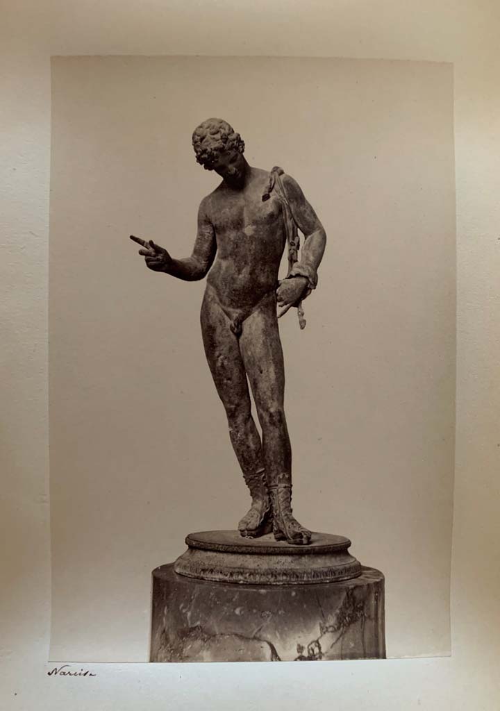VII.12.17.21 Pompeii. Photograph by M. Amodio, from an album dated April 1878.
Statuette of Narcissus also sometimes described as Dionysus or Pan. Photo courtesy of Rick Bauer.
According to Kuivalainen, this statue (now in Naples Archaeological Museum, inv. no: 5003), had fallen from the upper floor.
“The condition is good, but the original base has been replaced, and the panther is lost.”
He comments –
“The male’s apparel and the position of the right-hand fingers identifies the bronze as Bacchus dangling a bunch of grapes above a panther.
The iconographic formula is also known from wall paintings in Pompeii.”
See Kuivalainen, I., 2021. The Portrayal of Pompeian Bacchus. Commentationes Humanarum Litterarum 140. Helsinki: Finnish Society of Sciences and Letters, (p.219, H14.)
.