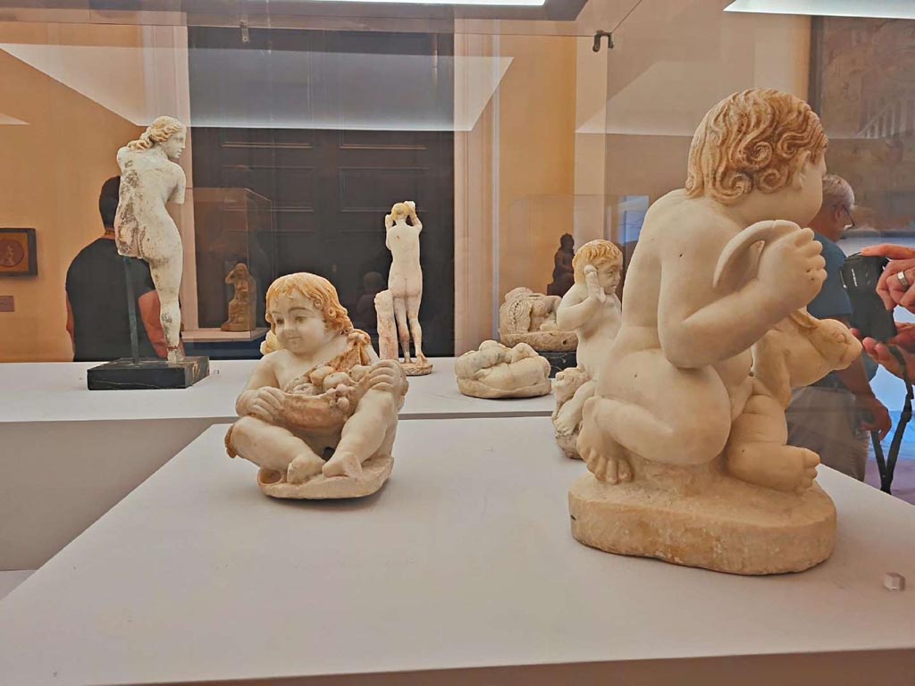 VII.12.23 Pompeii. October 2023. Group of statuettes, found in the garden area.
On the left – (10) Fountain figure of child holding fruits in his mantle, (inv. 6500).
On the right – (12) Fountain figure of a child holding up a hare, (inv. 6533).
At the rear – (11) Fountain figure of a child frightened by a toad, (inv. 6537).
Photo courtesy of Giuseppe Ciaramella.
On display in “L’altra MANN” exhibition, October 2023, at Naples Archaeological Museum.