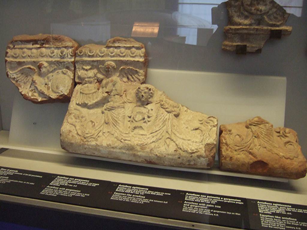 VIII.7.28 Pompeii. Temple pediment façade.
Moulded relief with two winged figures facing each other, one holding a shield and the other holding armour.
Vines fill the gaps below and a Dionysian head is superimposed. Now in Naples Archaeological Museum. Inventory numbers 21473, 21482, 21483.