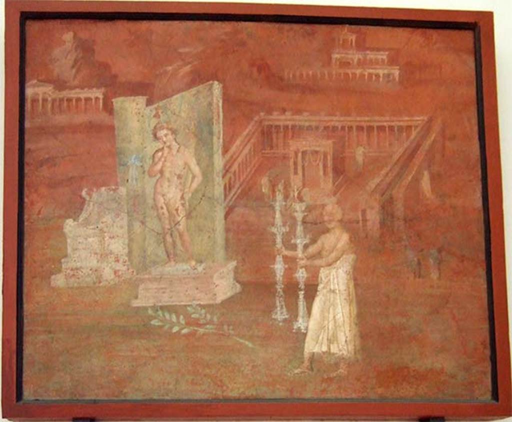 VIII.7.28 Pompeii. Painting found in niche on east wall.
It shows a montage of features concerned with the worship of Isis, including a statue of Harpocrates, a boy with a finger in his mouth holding a cornucopia, with a lotus blossom resting on his forehead.
Before him stands a priest in a long white robe with a candlestick in each hand.
In the background is a temple surrounded by a colonnade.
See Mau, A., 1907, translated by Kelsey, F. W., Pompeii: Its Life and Art. New York: Macmillan. (p. 172).
Now in Naples Archaeological Museum. Inventory number 8975.