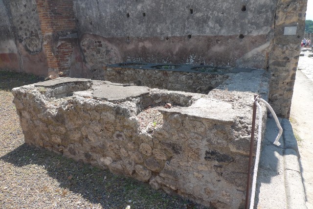 IX.1.8 Pompeii. December 2007. Room in north-east corner. Looking east. This room also contained the latrine, and a lararium, according to Fiorelli. According to Boyce, the lararium was on the east wall painted on a white background with a red border. In the middle, two serpents raised their heads, one on either side of a tile embedded in the wall and projecting out as a shelf for offerings. Two Lares were above the serpents, one on either side, wreathed, wearing red tunic and green pallium and holding rhyton and patera. In the middle below the serpents was a kantharos with a small bird perched on its rim.
See Boyce G. K., 1937. Corpus of the Lararia of Pompeii. Rome: MAAR 14. (p.79)