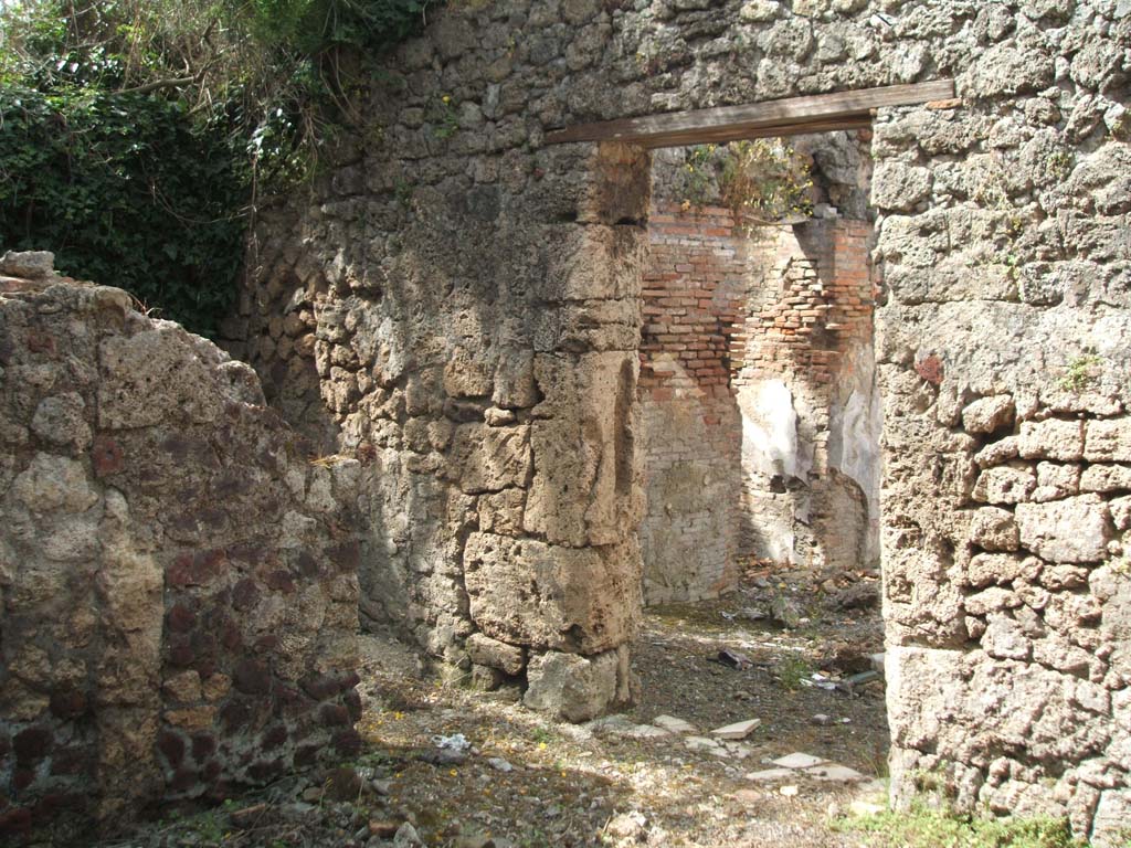 IX.7.19 Pompeii. May 2005.
Looking south-west from room g, towards doorway in south wall into room h, and in west wall leading into room b, the atrium, on right.
According to Mau, the best conserved parts of the floor in room g, showed that the couches were for at least twelve persons.
They had leaned against the rear wall, and against the rear right and rear left wall.
The decoration was the same as in the atrium, also with a white background, but simpler and without paintings.
The door closed from the internal part by half a beam, inserted in two holes in the doorpost, the one on the right a little higher than the other.
The doorway in the south wall, on the left, leads into room h, a cubiculum.
According to Mau, the cubiculum was not accessible other than from room g.
In this doorway there was no trace of either a threshold or hinges, and it seemed that the doorway had always remained open.
In the east wall, there was a small square window with an impression of a wooden window-frame.
The decoration, on white background and of the same style as that of rooms b and g, contained the following –
Left (west) wall – (size: conserved height 1.0m x conserved length 0.64m) country scene on a white background, showing a rural shrine shaded by a sacred tree, surrounded by a yellow balustrade with a broken herm of Priapus and a thyrsus, leaning against it. There were also two other unknown figures
Entrance (north) wall near the door, pendant to no.1. (size: height I.15m x length 0.76m) the other country scene showed the usual shrine shaded by a tree and in front of this above a pedestal was an image in bronze of a crowned Hercules, with his lion skin and his club on his left arm, and drinking cup in his outstretched right hand. In front of the image stood a man and a burning altar. At the back, there was a bridge with two goats on it.
Entrance (north) wall, to the right of no.2: fragment, (size: height 0.11m x length 0.44m) – Fishes and shells.
Left side of left (west) wall (size: height 0.175m x length 0.325) – A bird with some cherries, and above a shelf some other fruits, but only two were visible on the left, perhaps apples? (The rear part of the painting had vanished).
Right side of left (west) wall, pendant to no.4, (hardly conserved), fruit in two places, at least another fruit but not distinguishable.
See Mau, Bullettino dell’Instituto di Corrispondenza Archeologica (DAIR), 1883, (p.80-81).
According to Sogliano in NdS, the paintings found in room h, were in the most part destroyed when excavated. Two country scenes remained, one on the west wall which was damaged on the left side of it – see no.1 above, and the other country scene on the extreme west of the north wall - see no.2 above.
See Notizie degli Scavi di Antichità, 1880, (p.491).