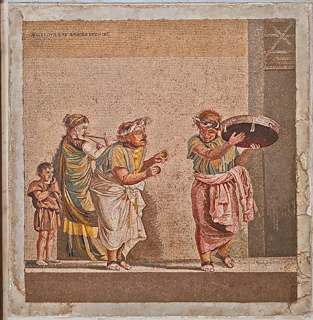 HGW06 Pompeii. Found on 8th April 1763. Ambiente 13 of Villa of Cicero.
Mosaic of a Group of Street Musicians. It bears the signature of Dioskourides of Samos.
Now in Naples Archaeological Museum. Inventory number 9985.
According to the information card –
Street musicians.
Mosaic emblema in opus vermiculatum made from polychrome tesserae, signed by Dioskourides of Samos.
The scene, inspired by the New Comedy, depicts three itinerant musicians with their faces covered by masks:
a musician playing cymbals in the centre, another with a tambourine to the right and a woman with a double flute to the left.
A boy on the left follows the procession. (Late 2nd – early Ist century BC.)
(I musici ambulanti.
Emblema pavimentale in opus vermiculatum di tessere policrome, firmato da Dioskourides di Samo.
La scena, ispirata alla Commedia Nuova, raffigura tre suonatori ambulanti col volto coperto da maschere:
un suonatore di cembali, al centro; un altro con tamburello, a destra; una donna col doppio flauto, a sinistra.
Un fanciullo, a sinistra, segue il corteo. Fine del II – inizi del I secolo a.C.)
Photo courtesy of Giuseppe Ciaramella. September 2024.