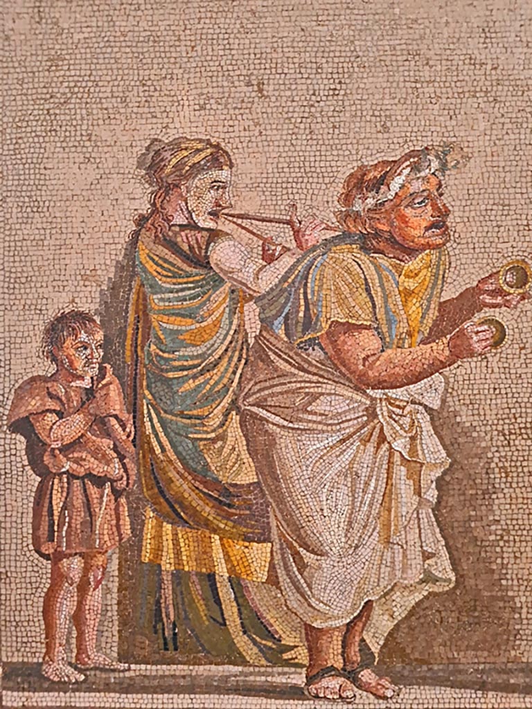 HGW06 Pompeii. Found on 8th April 1763. Ambiente 13 of Villa of Cicero.
Detail from mosaic of a Group of Street Musicians –
a musician playing cymbals on the right, in the centre a woman with a double flute, and on the left, a boy follows the procession.
Now in Naples Archaeological Museum. Inventory number 9985.
Photo courtesy of Giuseppe Ciaramella. September 2024.