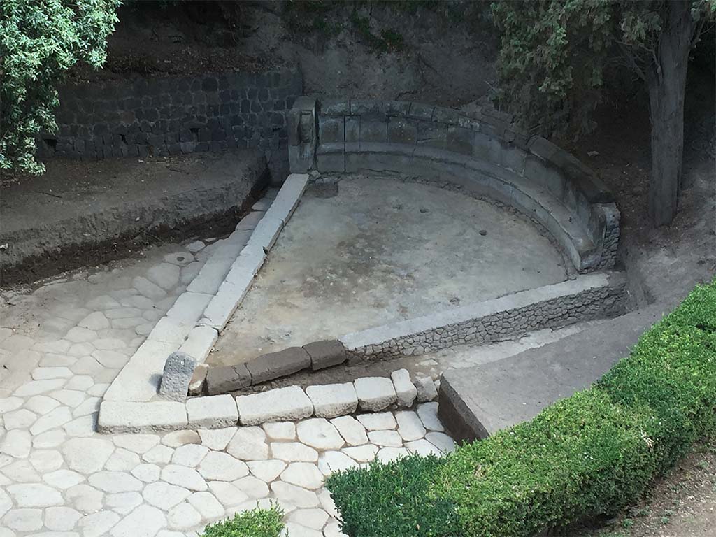 NGH Pompeii. 2015. Schola tomb after clearance showing previously covered tomb and basalt block roads. 
The continuation of ancient Via di Nola into unexcavated area is on the left.
The area immediately outside of Porta Nola (the Nolan Gate) was first cleared in 1907�8. 
Since then, soil had once again accumulated opposite the gate, re-burying the tomb. 
In 2015 the Porta Nola Project has cleared the basalt block roads and brought the monument back to light.
Excavation inside the monument in front of the benches revealed a thick layer of floor preparation for the pavement which has since disappeared.
See BSR Pompeii Project Porta Nola Necropolis 2015 Excavations
