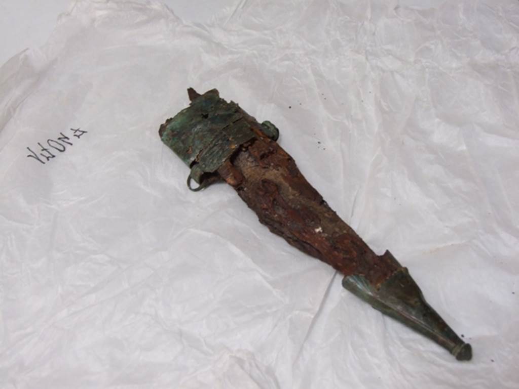 Nola Gate Tombs, Pompeii, March 2009. View from left. Large iron knife in a wooden sheath with bronze at the top and bottom. SAP inventory number 17047.
Found with Man no. 5 near Porta Nola in 1976.
