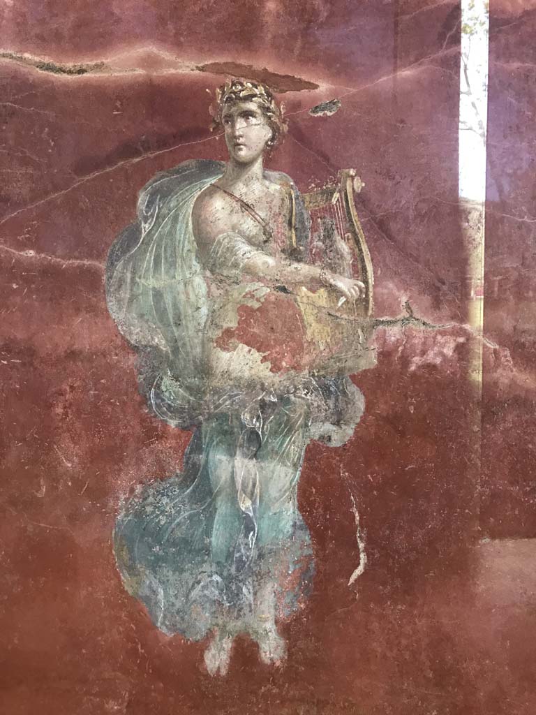 Complesso dei triclini in località Moregine a Pompei. April 2019. Triclinium A, north wall, Apollo with cithara.
Photo courtesy of Rick Bauer.
This has also been suggested as Erato, the Muse of lyric poetry, particularly erotic poetry, and mimic imitation, who is often depicted with a wreath of myrtle and roses, and holding a lyre, or a small kithara, a musical instrument often associated with Apollo.