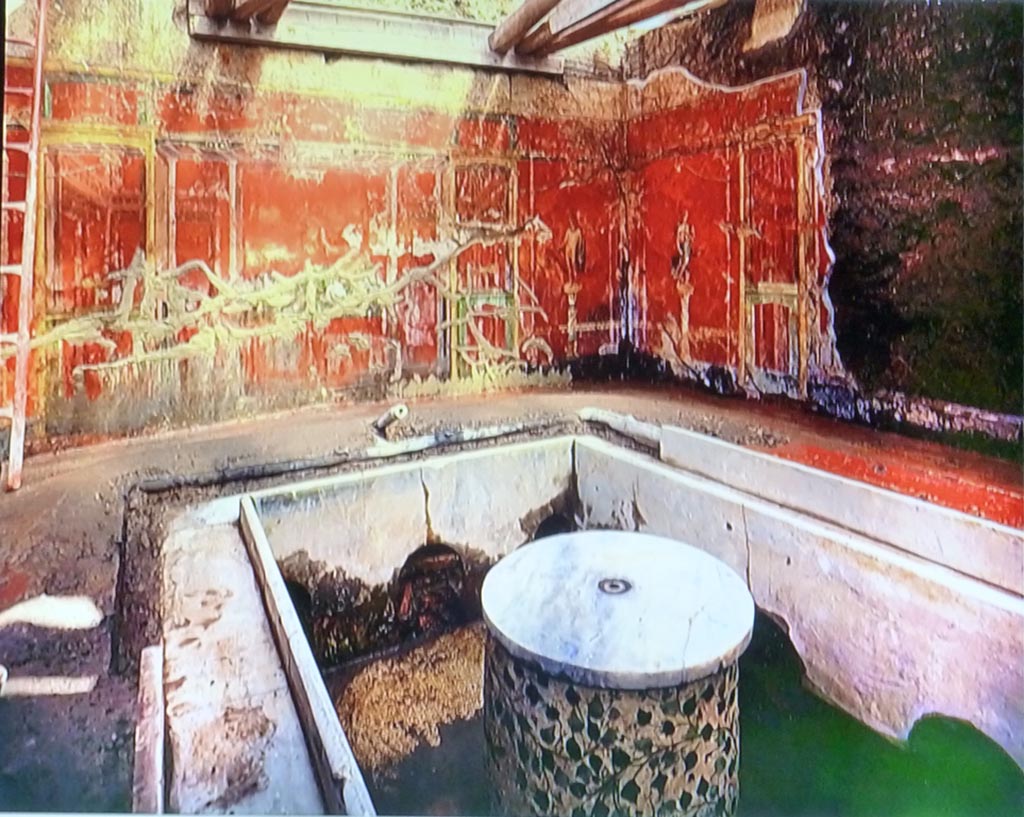 Complesso dei triclini in località Moregine a Pompei. 1959 excavation photo. On display in Pompeii Palaestra September 2015.
Triclinium C. North and east walls in situ with marble clad triclinium and round table with plant decorations.
Water channels run around the sides of the triclinium and remains of a water jet can be seen at the rear.
Water was a problem during excavation as the complex was below the water table after the eruption, though this had also helped preserve some items.